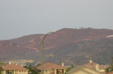 Larry Himmel, a television reporter, did a report in front of his burning house. His house was out on that hill somewhere. At the top of the hill you can see some trees. There used to be a large blue house where those trees are. At the far left you can also see a fuzzy silhouette of a destroyed home.
(John Vogel)