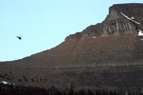 
                    A helicopter heads up to rescue an injured hiker on Going to the Sun Mountain. In the left-hand corner, one can see the diagonal snow chute marking where the hiker fell.
                                            (Michael May)
                                        
