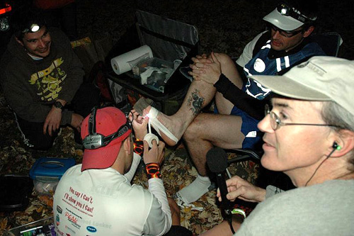 
                    At one of the makeshift aid stations along their long route, John tries to tape Nate's fallen arch to give him some support so he can continue.
                                            (Sarah Chretien)
                                        